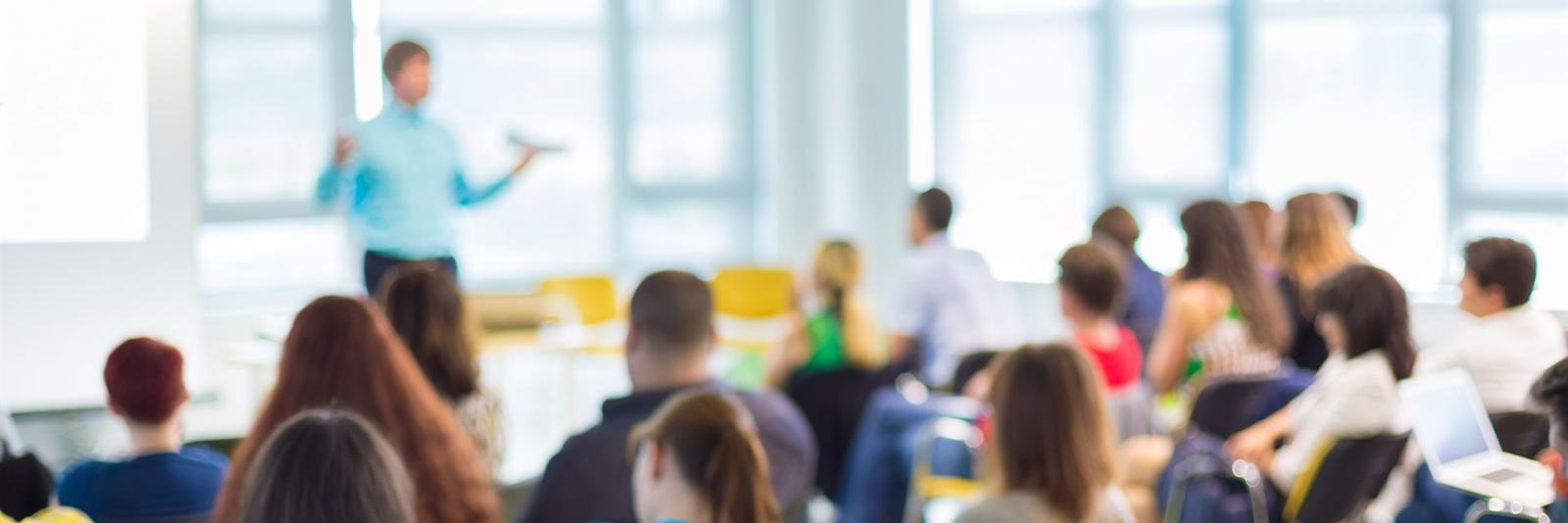 Workshops organisieren & vermarkten – FM-Connect.com Expert steht vor aufmerksamen Teilnehmern und Dozenten auf einem Workshop im Bereich des Facility Management (unscharfes Foto)