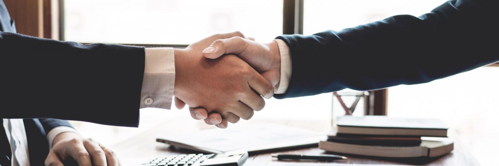 Facility Management - Beratung & Netzwerk Zwei Experten reichen sich die Hand am Bueroarbeitsplatz