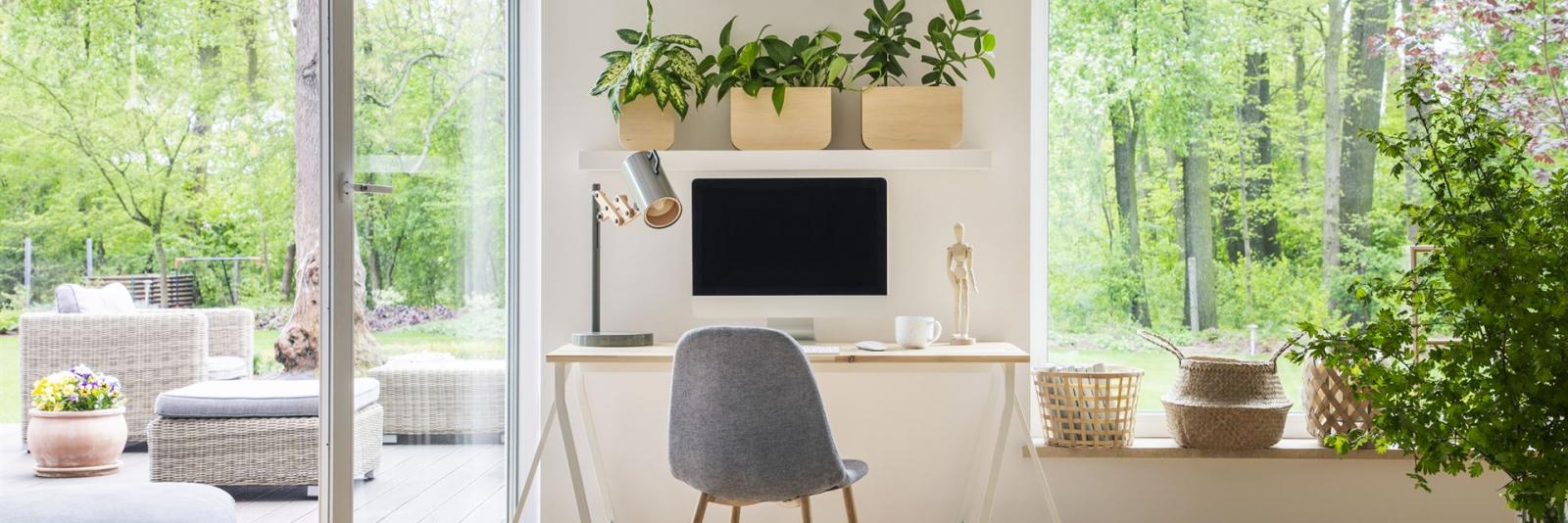 Verwaltung von externen Arbeitsplätzen – Facility Management Innenansicht eines gemutlichen dekorierten Homeoffice-Arbeitsplatzes mit Blick ueber einen Garten mit Gartenmoebeln
