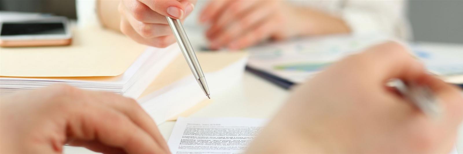 Expertin zeigt ihrem Geschaeftspartner mit einem Kugelschreiber, wo er unterschreiben soll