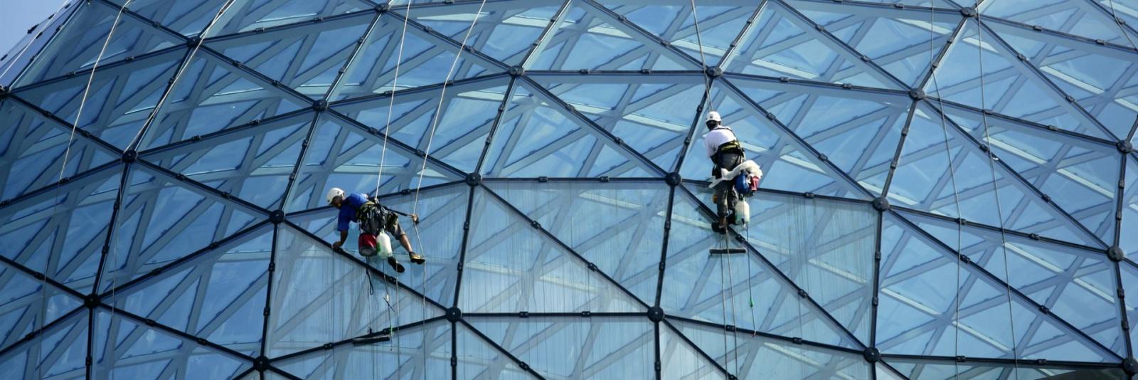 Routinemäßige Leistung in periodischen Zeitintervallen bei einer FM-Organisation Reinigungspersonal mit Seilen gesichert machen Reparaturen und putzen die Glasfassade eines Kuppelbaus