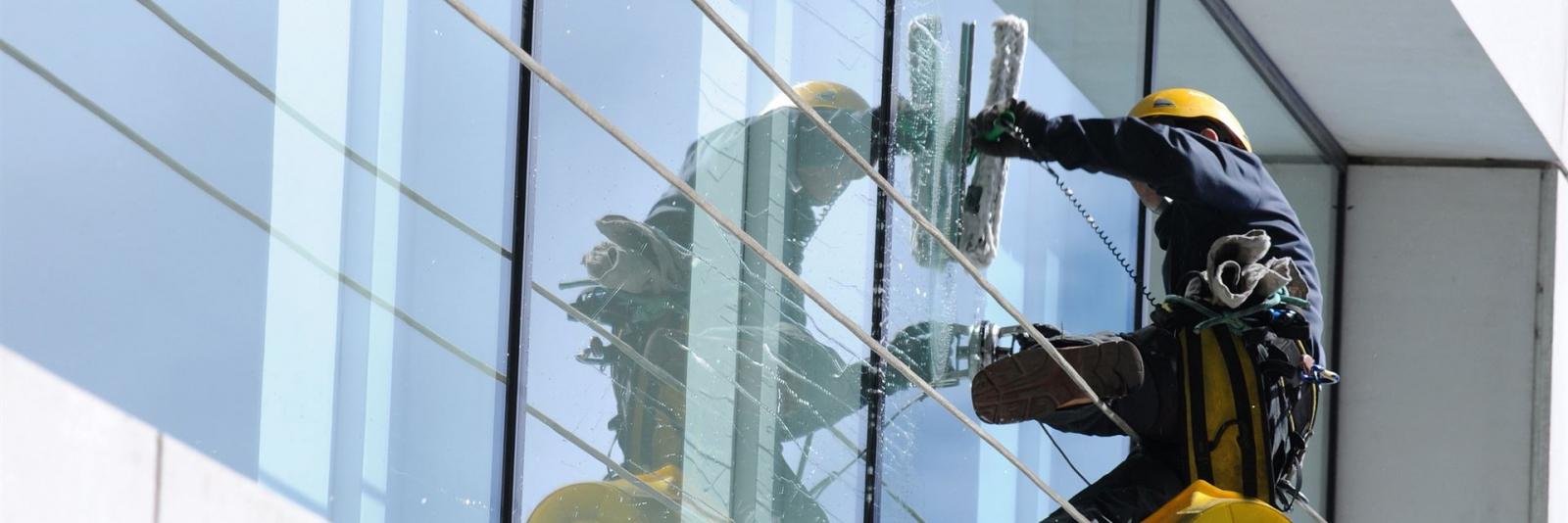 Reinigung und Erhaltung von Vermögenswerten bei einer FM-Organisation Arbeiter reinigt die Glasfassade eines Buerogebaeudes unter der Einhaltung der Sicherheitsmaßnahmen