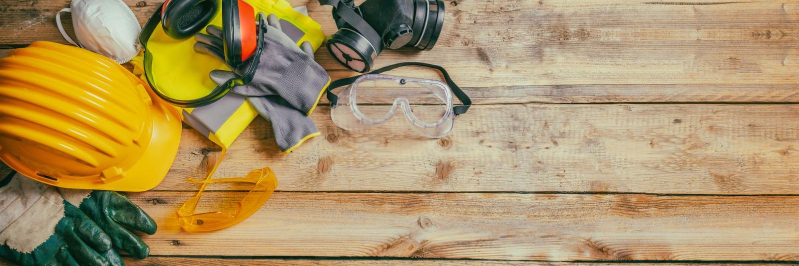 Gesundheit & Sicherheit am Arbeitsplatz – Facility Management Sicherheitsausrüstung fuer Bauarbeiten liegt auf Holzfußböden wie z.B. Schutzhelm, Schutzbrille, Schutzhandschuhe, unter anderem