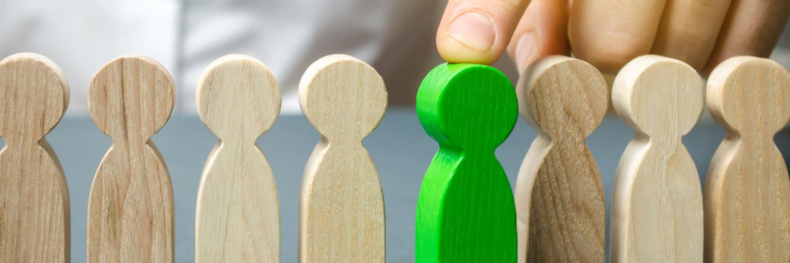 Personalwesen bei einer FM-Organisation Expert waehlt mit seinem Zeigefinger eine gruene menschliche Figur aus Holz aus