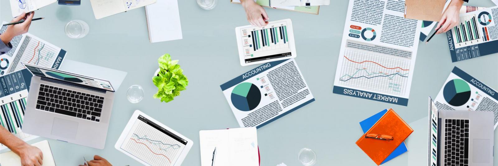 Ressourcen- & Leistungsermittlung im Facility Management Bueroarbeiter am Arbeitstisch mit zahlreichen notwendigen Arbeitsmitteln wie Berichte, Abbildungen, Tabellen, Laptops, usw.
