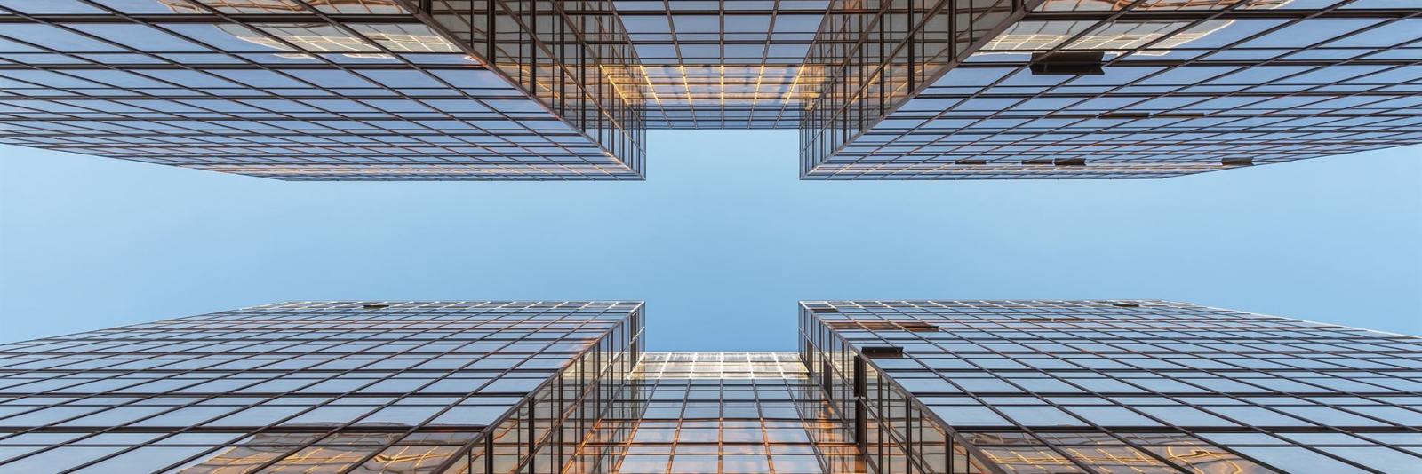 Berücksichtigung von Flächen- & Ausstattungsstandards im Facility Management Ansicht von unten nach oben eines Buerokomplexes mit Glasfassade mit voellig klarem Himmel