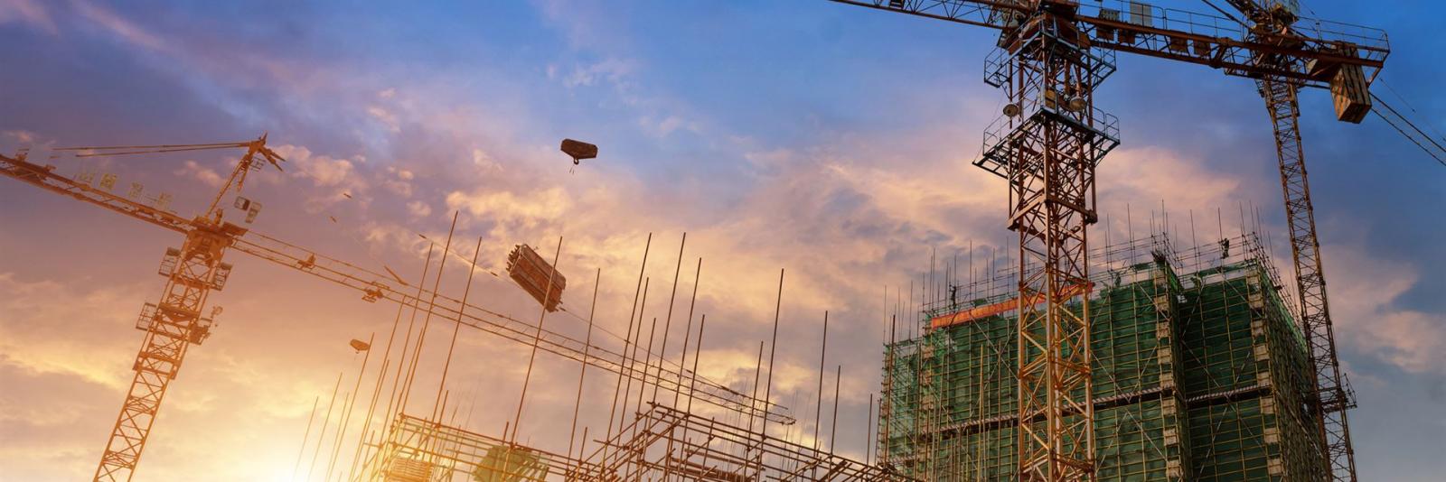 Steuern von Bauprojekten (LzPh. 1) – Facility Management Ansicht von unten einer Baustelle mit unfertigen Objekten und drei Kranen in Betrieb