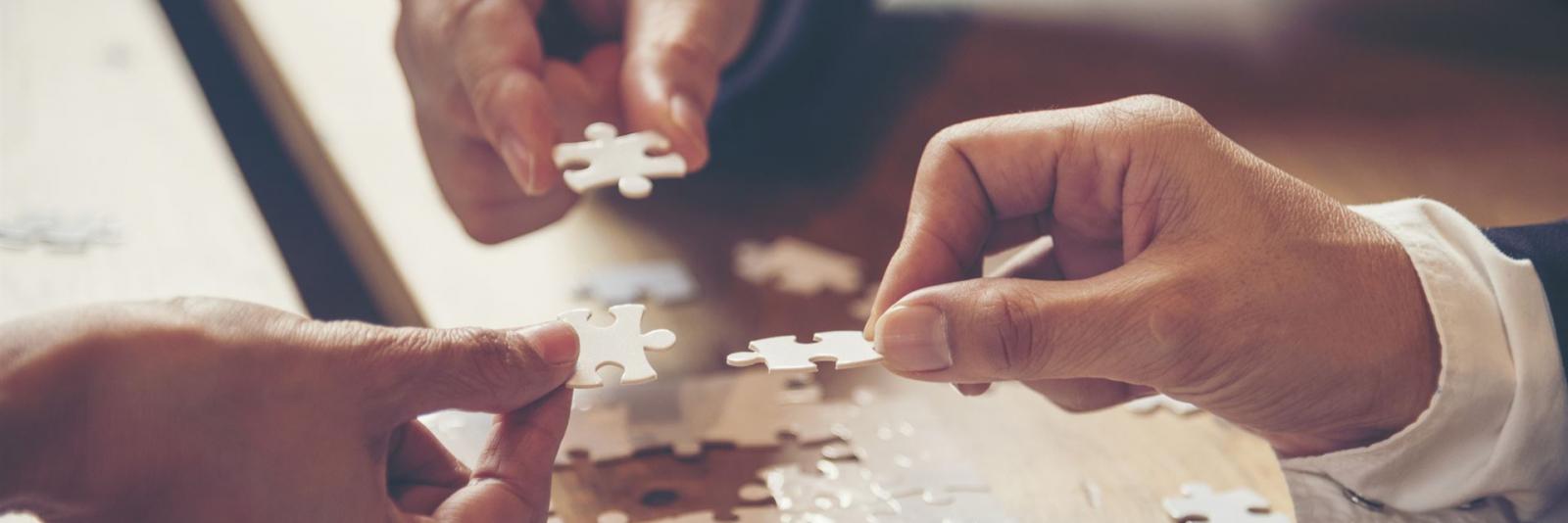 Partnerschaft für gute Geschäfte beim Facility Management Drei Experten setzen weisse Puzzleteile mit ihren rechten Haenden zusammen